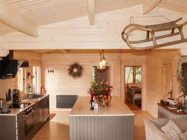 A kitchen with wooden walls and ceiling a central island with flowers and a bottle a wooden sled hanging from the ceiling at Gardeners Lodge in Huby