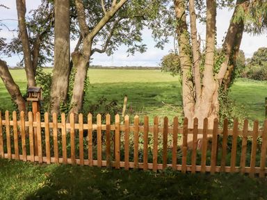 A wooden fence with trees and a birdhouse in front of a grassy field at Gardeners Lodge in Huby