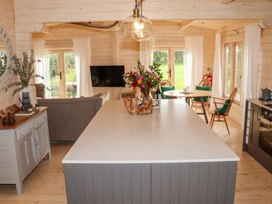 An open living space with a kitchen island, dining table, sofa, and television at Gardeners Lodge in Huby