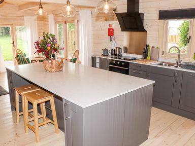 A kitchen with a large island with flower vase and two stools a dining table with chairs and large windows at Gardeners Lodge in Huby