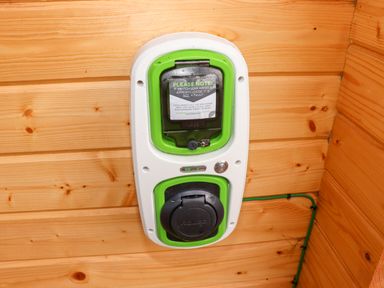 An electric vehicle charging point mounted on a wooden wall at Gardeners Lodge in Huby