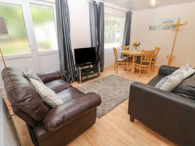 A living room with two leather sofas a small TV on a stand a round dining table with chairs and a coat rack at 11 Tremore in Liskeard