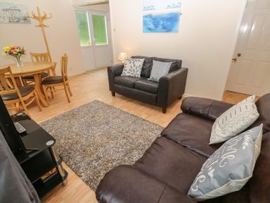 A living room with two leather sofas a wooden dining table with chairs a coat rack and a rug at 11 Tremore in Liskeard