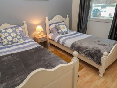 A bedroom with two single beds a nightstand lamp and a window at 11 Tremore in Liskeard