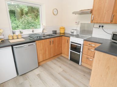 A kitchen with wooden cabinets a window above the sink and various appliances at 11 Tremore in Liskeard