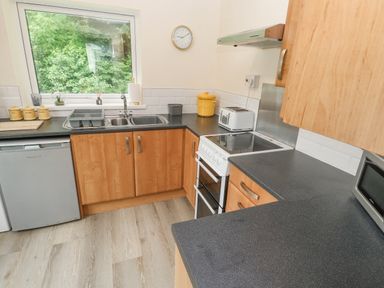 A kitchen with wooden cabinets a sink a stove a toaster and a window showing greenery at 11 Tremore in Liskeard