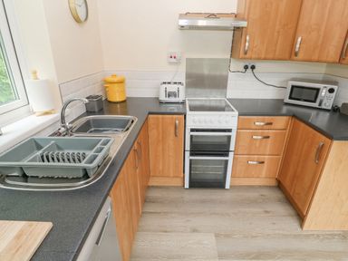 A kitchen with wooden cabinets a white oven a microwave a toaster a sink with a dish drainer and a yellow bread container at 11 Tremore in Liskeard
