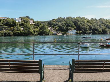 Two benches facing a body of water with boats and houses on a tree-covered hillside at 11 Tremore in Liskeard