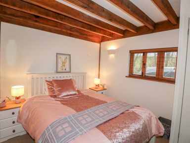 A bedroom with a bed with pink bedding two bedside tables with lamps and a window with wooden blinds at Honeypot Lodge in Camelford