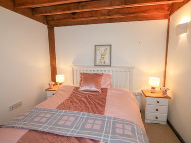A bedroom with a bed between two bedside tables with lamps and a picture of a rabbit above the bed at Honeypot Lodge in Camelford