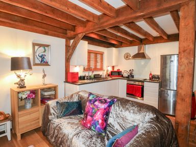 A kitchen and seating area with wooden beams white cabinets and colorful cushions at Honeypot Lodge in Camelford