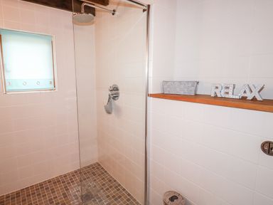 A tiled shower area with a glass door and a shower head above at Honeypot Lodge in Camelford