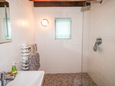 A bathroom with a sink a towel rack with towels a shower area with a glass partition and a window at Honeypot Lodge in Camelford