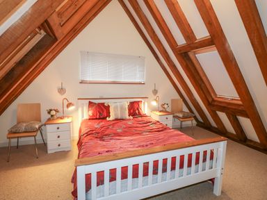 A bedroom with a double bed red bedding wooden beams and two bedside tables at Honeypot Lodge in Camelford