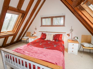 A bedroom with a bed between two nightstands under a sloped ceiling with wooden beams at Honeypot Lodge in Camelford