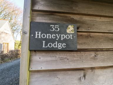 A wooden wall with a sign displaying 35 Honeypot Lodge and a small beehive illustration at Honeypot Lodge in Camelford