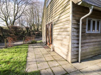 Exterior view of a wooden house with a paved patio and grass lawn at Honeypot Lodge in Camelford