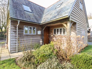 Exterior of a wooden house with plants and shrubs near the entrance at Honeypot Lodge in Camelford