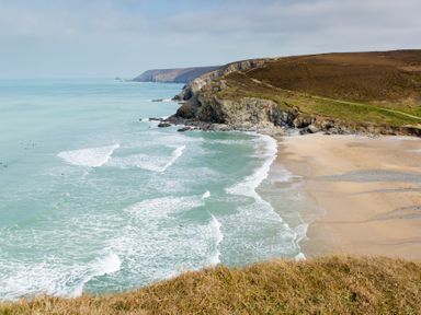 A coastline with waves crashing on a sandy beach and rocky cliffs at Honeypot Lodge in Camelford