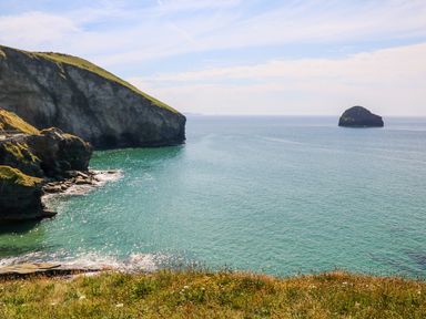 A coastal view with rocky cliffs and an island in the sea at Honeypot Lodge in Camelford