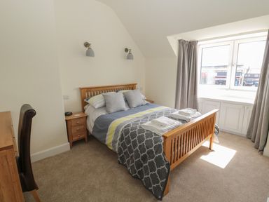 A bedroom with a wooden bed frame with pillows and folded towels near a window with curtains at Hazonleigh in Seahouses