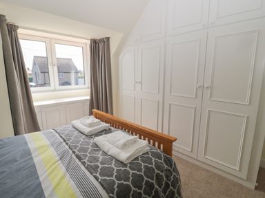 A bedroom with a wooden bed and folded towels on it with built in white wardrobes and a window with curtains at Hazonleigh in Seahouses