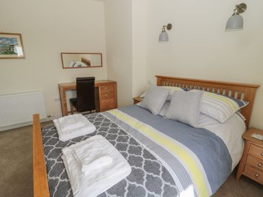 A bedroom with a wooden bed with striped bedding and towels on it a wooden desk with a chair a mirror a radiator and wall lights at Hazonleigh in Seahouses
