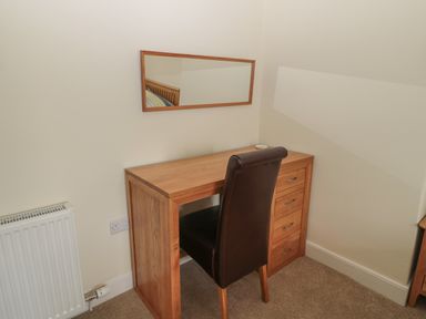 A wooden desk with drawers and a dark chair in a corner under a rectangular mirror in a room at Hazonleigh in Seahouses