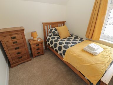 A bedroom with a single wooden bed and yellow bedding next to a window with yellow curtains and wooden drawers at Hazonleigh in Seahouses