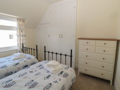 A bedroom with two single beds with patterned bedding a window with curtains built in wardrobes and a chest of drawers at Hazonleigh in Seahouses