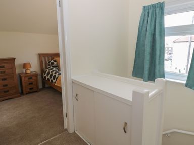 A hallway with a white storage cabinet and teal curtains with a bedroom visible with wooden furniture at Hazonleigh in Seahouses