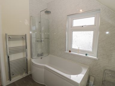 A bathroom with a bathtub shower combination a towel rack and a window with frosted glass at Hazonleigh in Seahouses