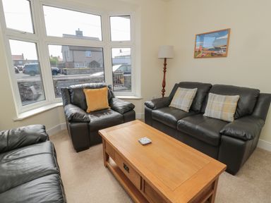 A living room with leather sofas a wooden coffee table a floor lamp and a framed picture on the wall at Hazonleigh in Seahouses