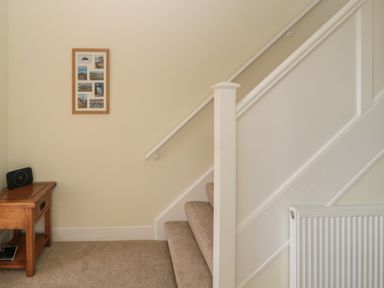 A staircase with carpeted steps next to a wooden side table with a speaker and framed pictures on the wall at Hazonleigh in Seahouses
