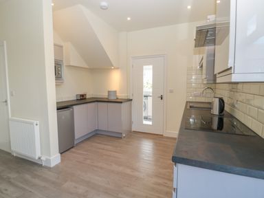 A kitchen with cabinets a stove kettle microwave and a door leading to a laundry room at Hazonleigh in Seahouses