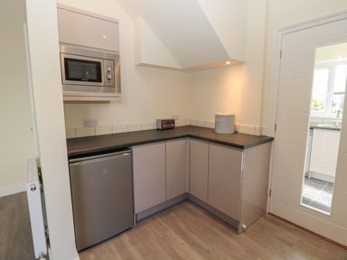 A small kitchen area with a microwave oven, mini refrigerator, countertop, cabinets, radio, and bread container at Hazonleigh in Seahouses