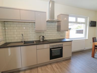 A kitchen with beige cabinets a black countertop a sink a kettle an oven and a window at Hazonleigh in Seahouses