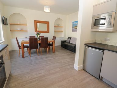 A dining area with a wooden table and brown chairs next to a black sofa and a kitchenette with a microwave and refrigerator at Hazonleigh in Seahouses