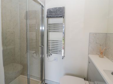 A bathroom with a shower enclosure a towel radiator with a towel a toilet and a sink with a reed diffuser at Hazonleigh in Seahouses