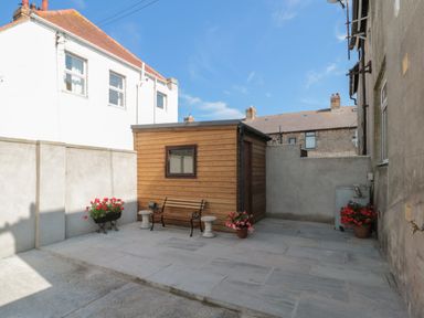 An outdoor patio area with a wooden shed a bench and potted plants at Hazonleigh in Seahouses