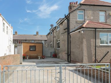A fenced driveway leading to a concrete yard with a wooden shed and a bench at Hazonleigh in Seahouses