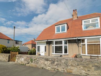 A semi detached house with a red roof and stone wall in front at Hazonleigh in Seahouses