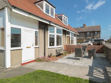 A front yard patio with outdoor chairs and a bench in front of a house at Hazonleigh in Seahouses