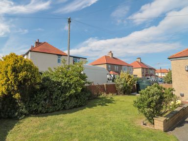 A front garden with shrubs grass and a brick wall near houses with red roofs at Hazonleigh in Seahouses