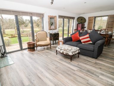 A living room with a gray sofa and red pillows an armchair a patterned ottoman and sliding glass doors overlooking a garden at Romsey Lodge in Wark