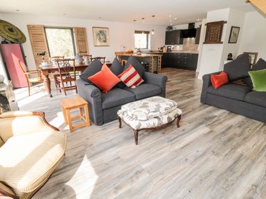 A living room with two gray sofas with cushions a patterned ottoman a wooden dining table with chairs and a kitchen area at Romsey Lodge in Wark