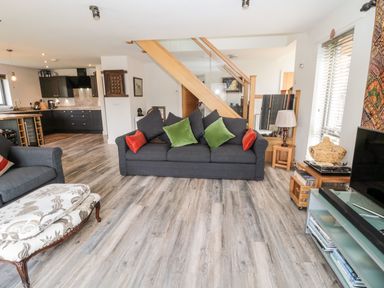 A living room with dark sofas with colored cushions a patterned ottoman wooden flooring and a kitchen area at Romsey Lodge in Wark