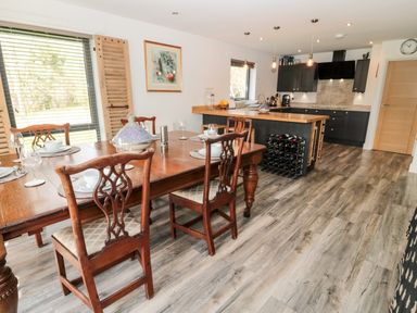 A dining area with wooden table and chairs next to a kitchen with dark cabinets and a wooden countertop at Romsey Lodge in Wark