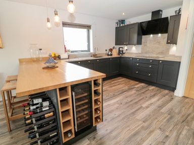A kitchen with black cabinets a wooden counter with wine bottles and stools at Romsey Lodge in Wark