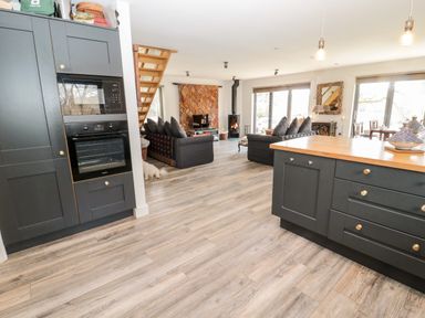 An open plan kitchen and living room with black cabinetry wooden countertops sofas a wood burning stove and large windows at Romsey Lodge in Wark